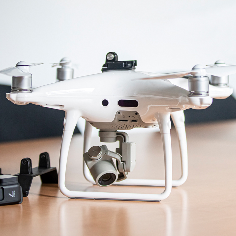 Weiße DJI-Phantom-Drohne mit Kamera am Gimbal auf einem Tisch, daneben Zubehör